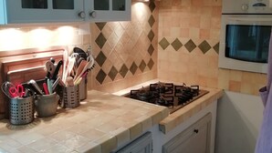 A kitchen with a gas stove, oven, and various utensils in holders. There are cabinets with glass doors and a tiled backsplash. - Quiet house near Nice (Contes)