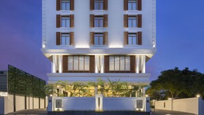 A modern multi-story building with a flat roof, large windows with wooden shutters, and a well-lit entrance area with plants. - The Residency Towers Puducherry (Puducherry)