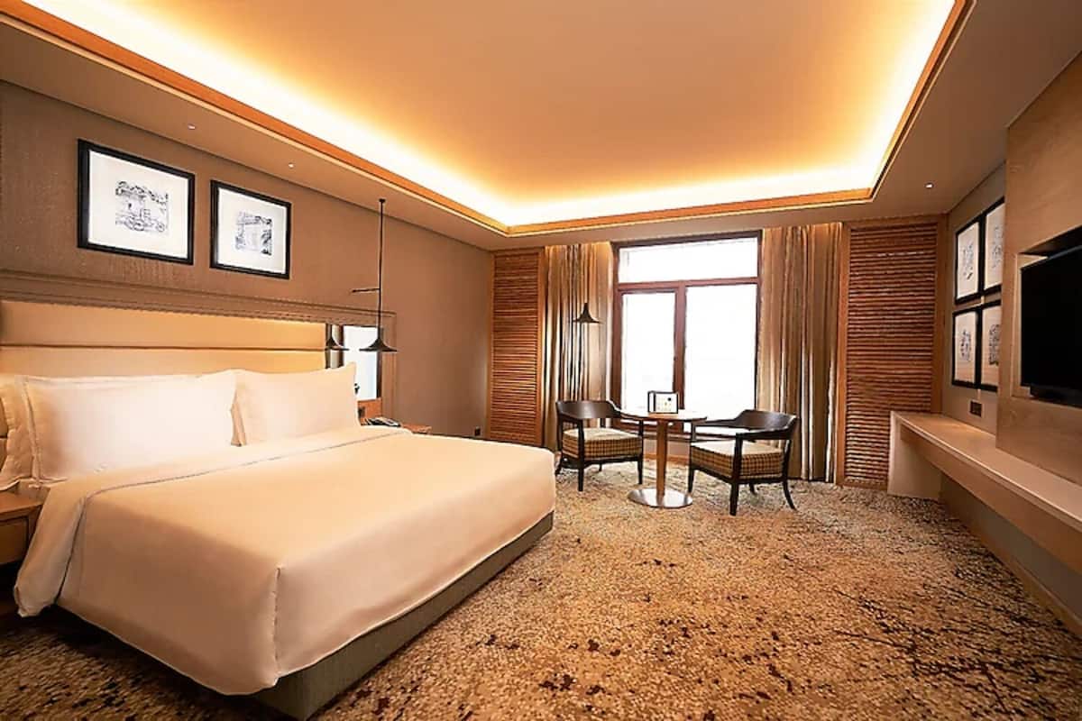 Une chambre d’hôtel avec un grand lit, un bureau avec deux chaises, une télévision et des tableaux encadrés aux murs.