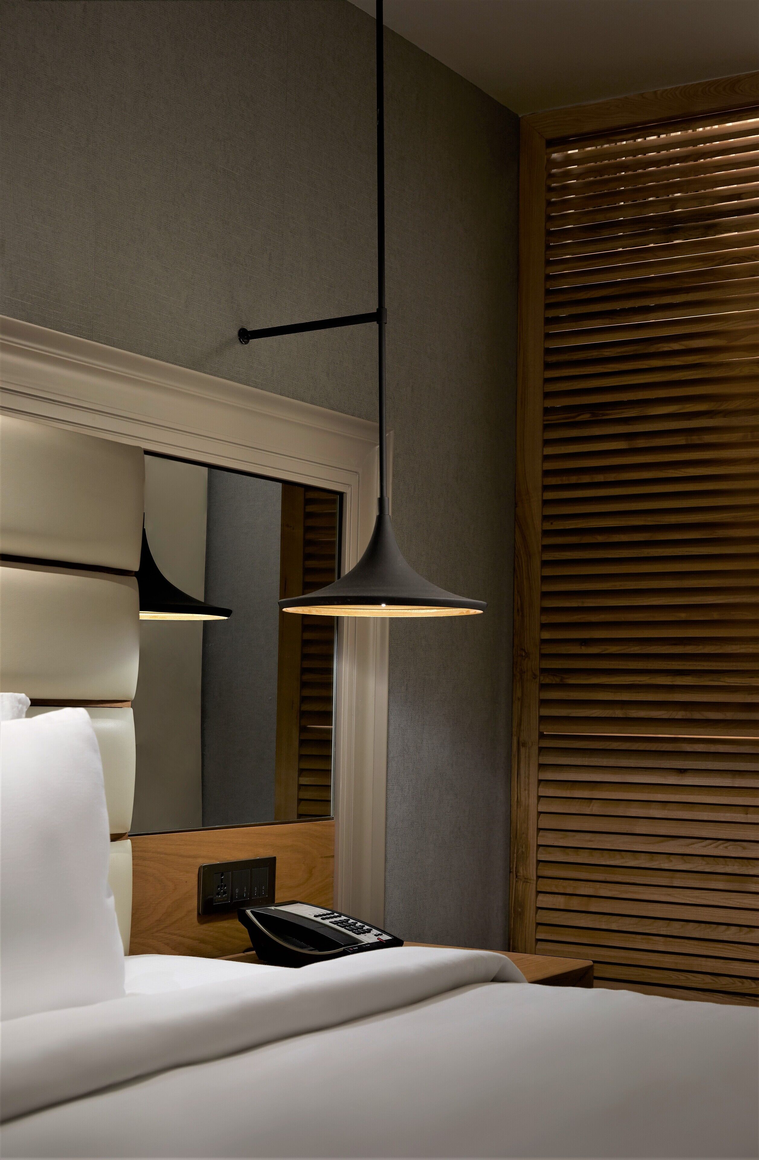 Una habitación de hotel con cama, teléfono en la mesita de noche y una lámpara colgante moderna.