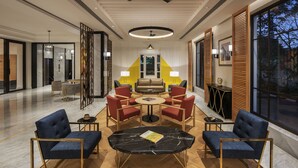 Um lobby de hotel moderno com área de estar central, ventilador de teto e grandes janelas.