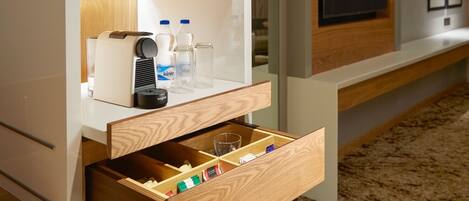 A modern hotel room with a built-in TV, minibar, and a wooden drawer unit.