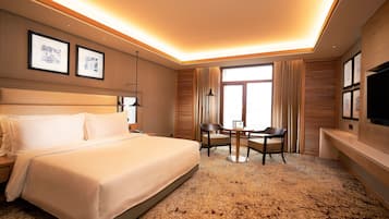 A hotel room with a large bed, a desk with two chairs, a flat-screen TV, and framed artwork on the walls.