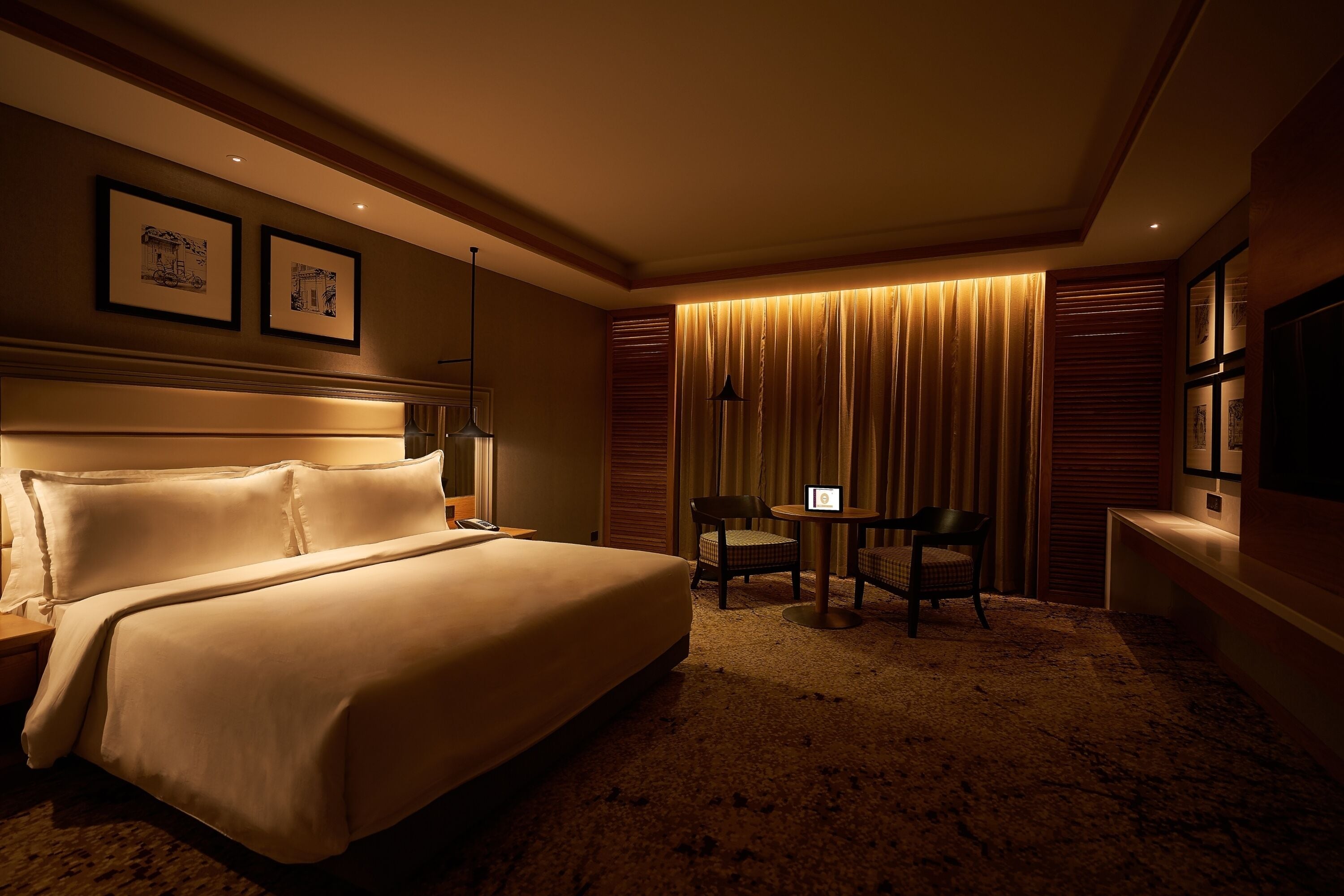 A hotel room with a large bed, a desk with a chair, a TV, and framed pictures on the wall.