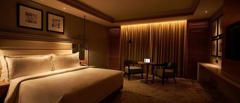 A hotel room with a large bed, a desk with a chair, a TV, and framed pictures on the wall.