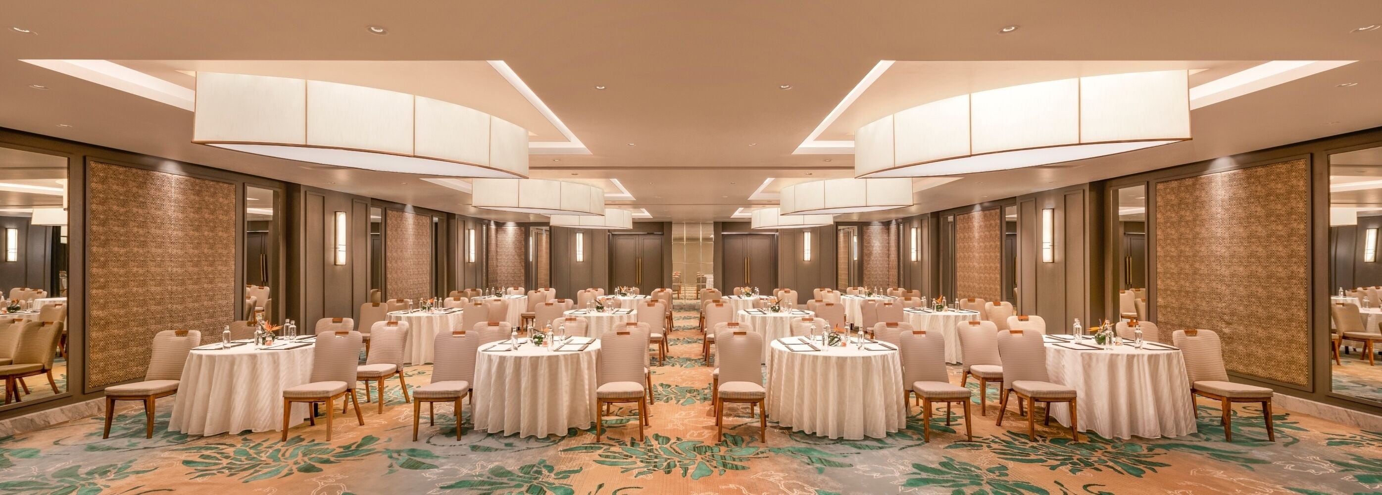 A large banquet hall with round tables and chairs, high ceilings, and patterned carpet.