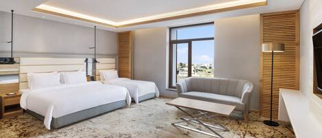 Une chambre d’hôtel moderne avec deux lits, un canapé, une petite table et une grande fenêtre donnant sur la ville.