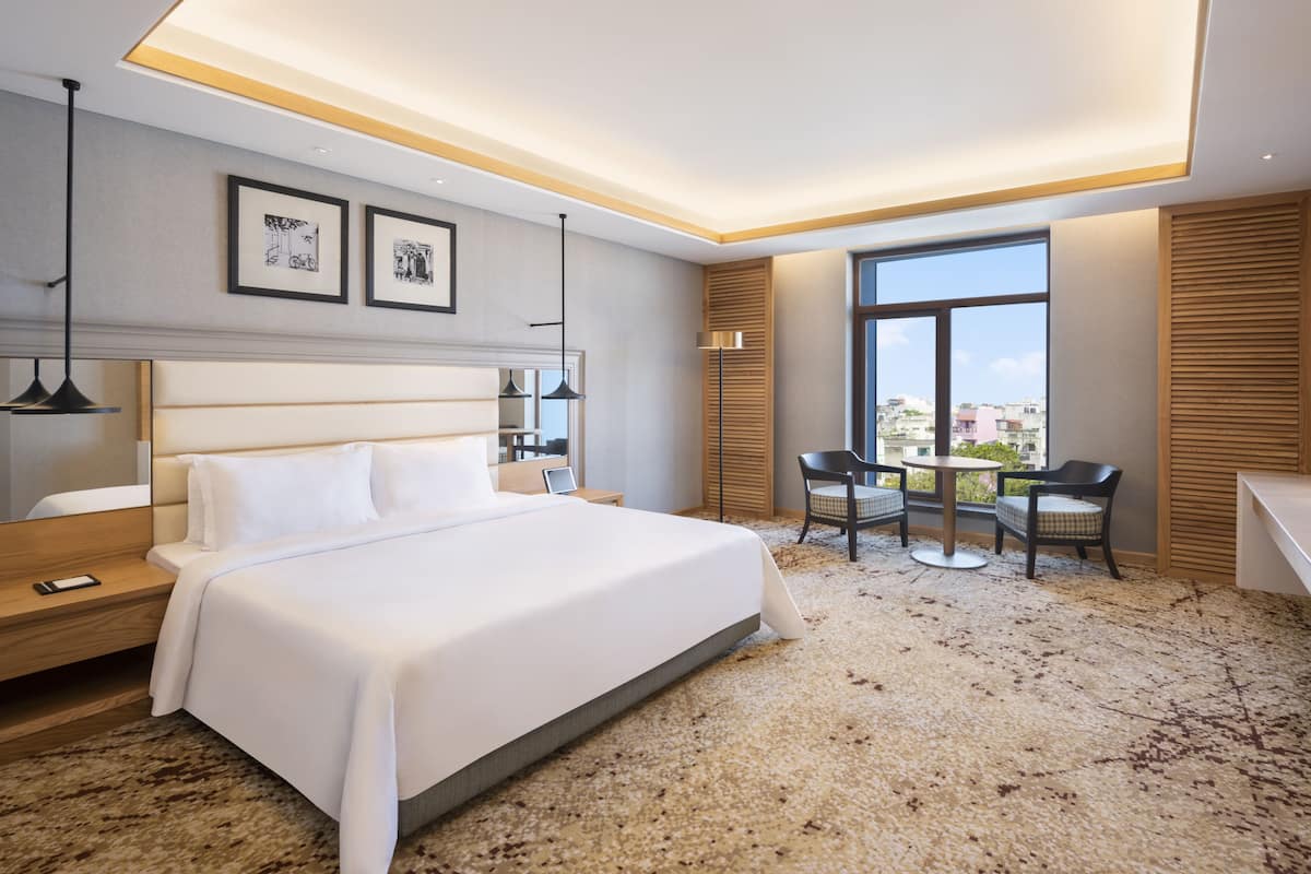Une chambre d’hôtel moderne dotée d’un grand lit, d’un bureau, d’une chaise, d’une télévision et d’un balcon offrant une vue sur la ville.