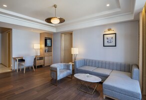 Una sala de estar moderna con un sofá gris, una mesa de centro redonda y un escritorio con una silla. Hay un armario de madera y una lámpara en el escritorio.