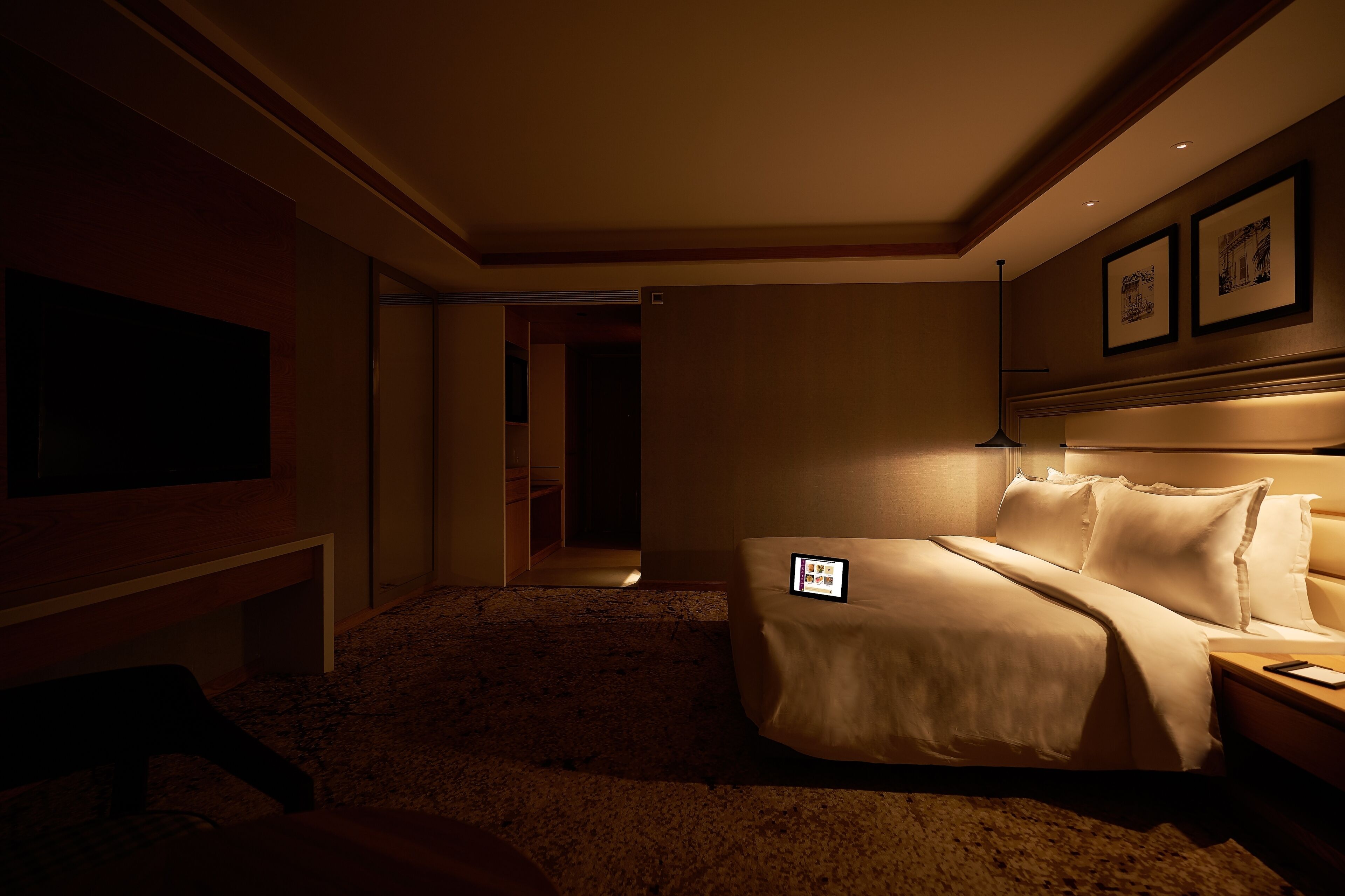 A hotel room with a bed, bedside table, lamp, and a TV on the wall.