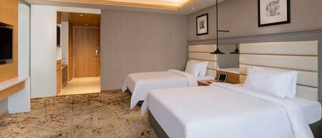 Habitación de hotel con dos camas, televisión, escritorio y piso alfombrado.