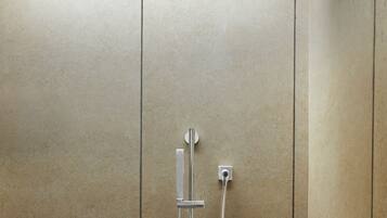 A shower with a handheld showerhead and a wall-mounted faucet, set against a tiled wall.