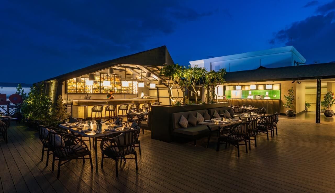 An outdoor dining area with tables and chairs, a bar area with stools, and a seating area with a sofa and chairs.