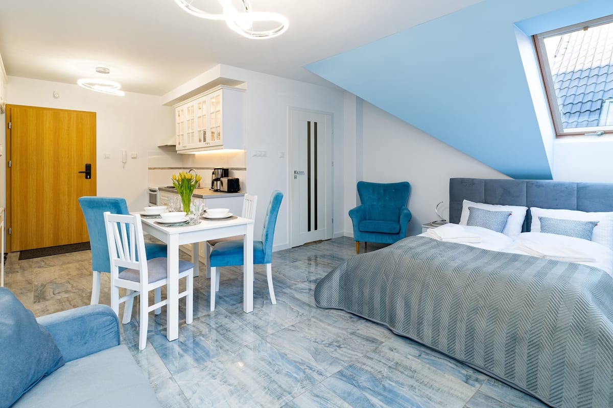 Ein modernes Hotelzimmer mit Essbereich, einer Küchenzeile, einem Bett mit Blick und einer blauen Akzentwand.