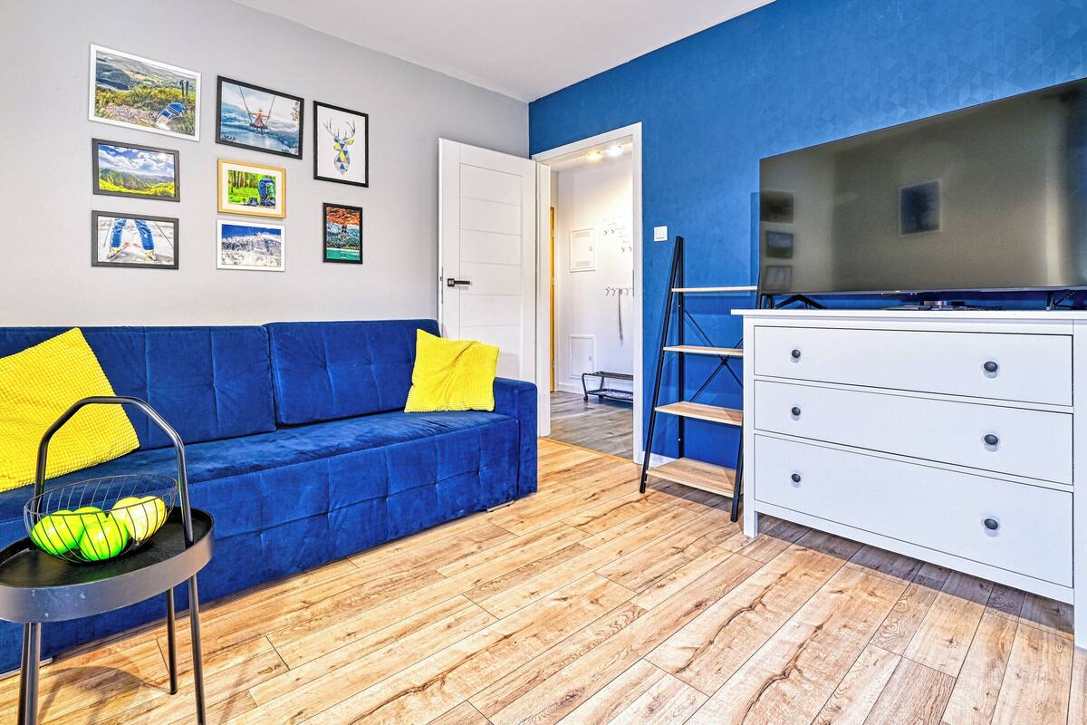 Ein modernes Wohnzimmer mit einem blauen Sofa, einer weißen Kommode und einem Fernseher auf einem Lowboard.