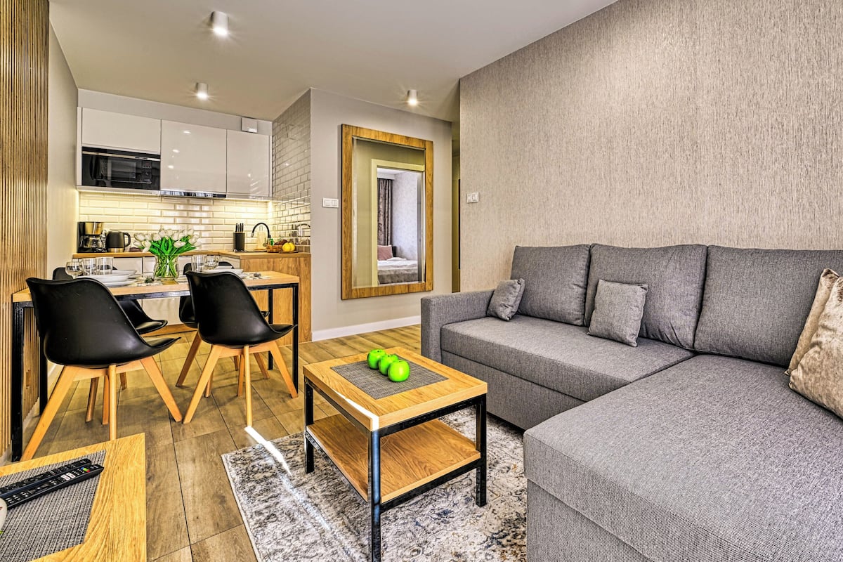 Ein modernes Wohnzimmer mit einem grauen Sofa, schwarzen Sesseln und einem Holztisch.