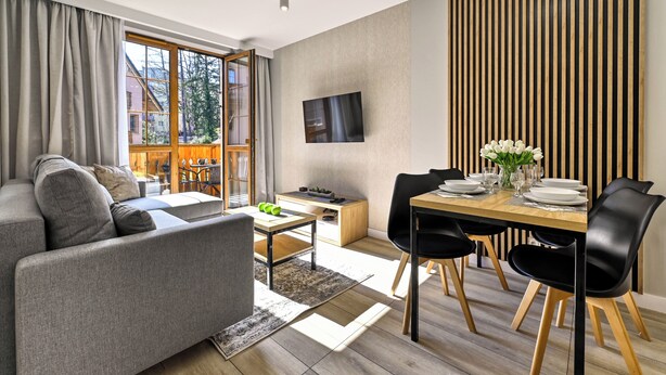 Een moderne woonkamer met een bank, een eettafel voor vier personen en een aan de muur bevestigde televisie.