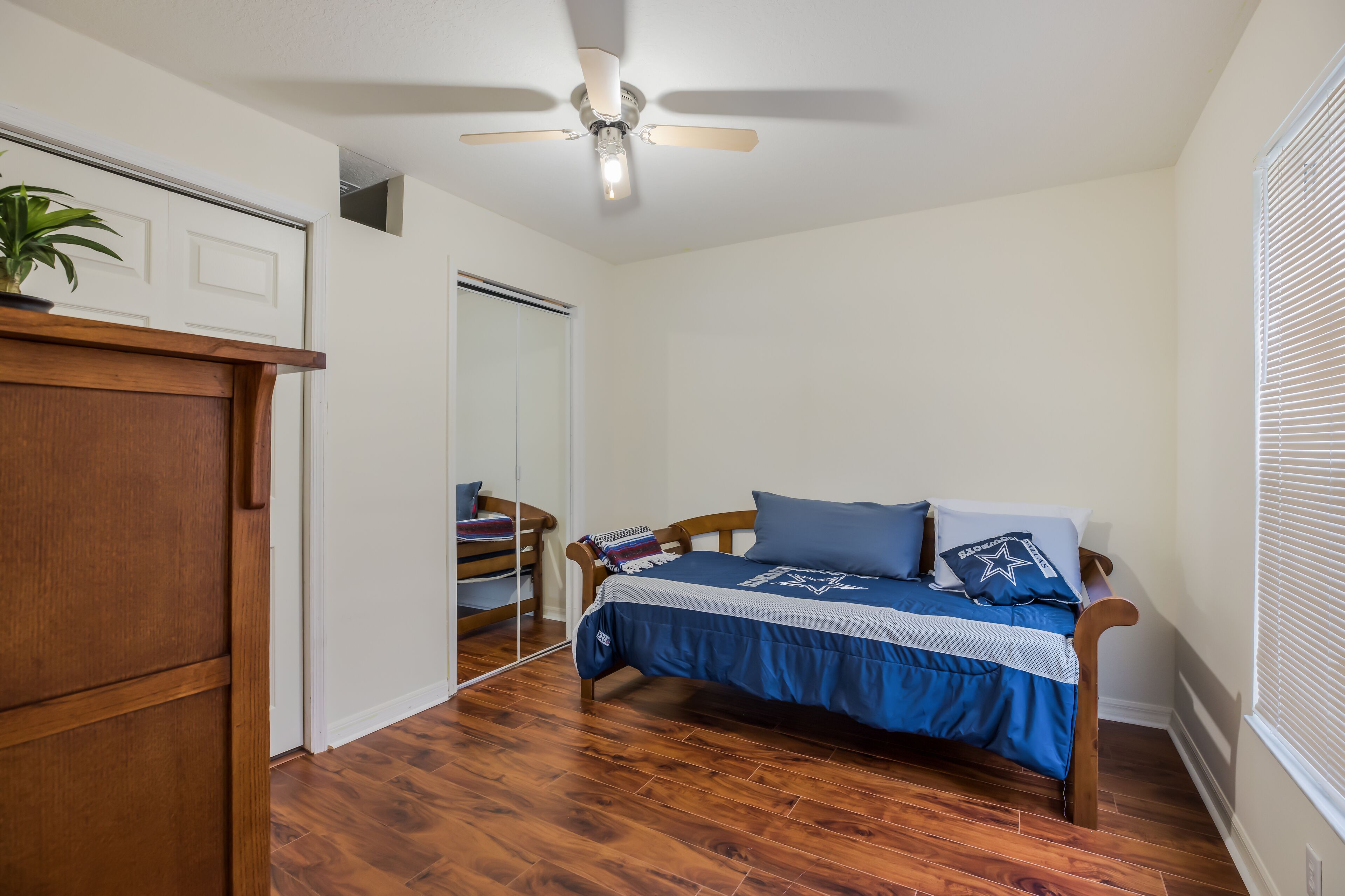 Un dormitorio con una cama de madera, un ventilador de techo y un armario.