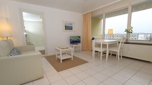 A modern living room with a sofa, a small table, a TV, and a dining area with chairs. - Metropol House, apt. 109 (Sylt)