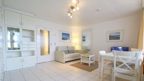 A spacious living room with a white sofa, a coffee table, and a dining area with a white table and chairs. - Metropol House, apt. 109 (Sylt)