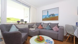A modern living room with a grey sofa, a round coffee table, and a painting of a lighthouse. - App. Kohfahl 65, Germany (Sylt)