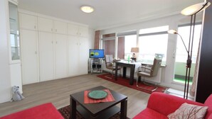 A spacious living area with a red sofa, a dining table with chairs, a television, and a cabinet. - Haus am Meer14-app 078a OB (Sylt)