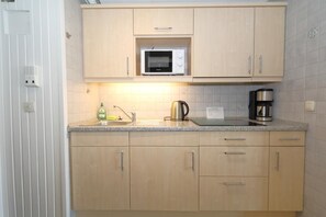 A kitchen with light wooden cabinets, a built-in microwave, a coffee maker, and a kettle on the countertop.