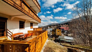A wooden balcony with a wooden table and chairs, overlooking a village with houses and mountains in the background. - Sun & Snow Centrum Obrońców Pokoju (Karpacz)