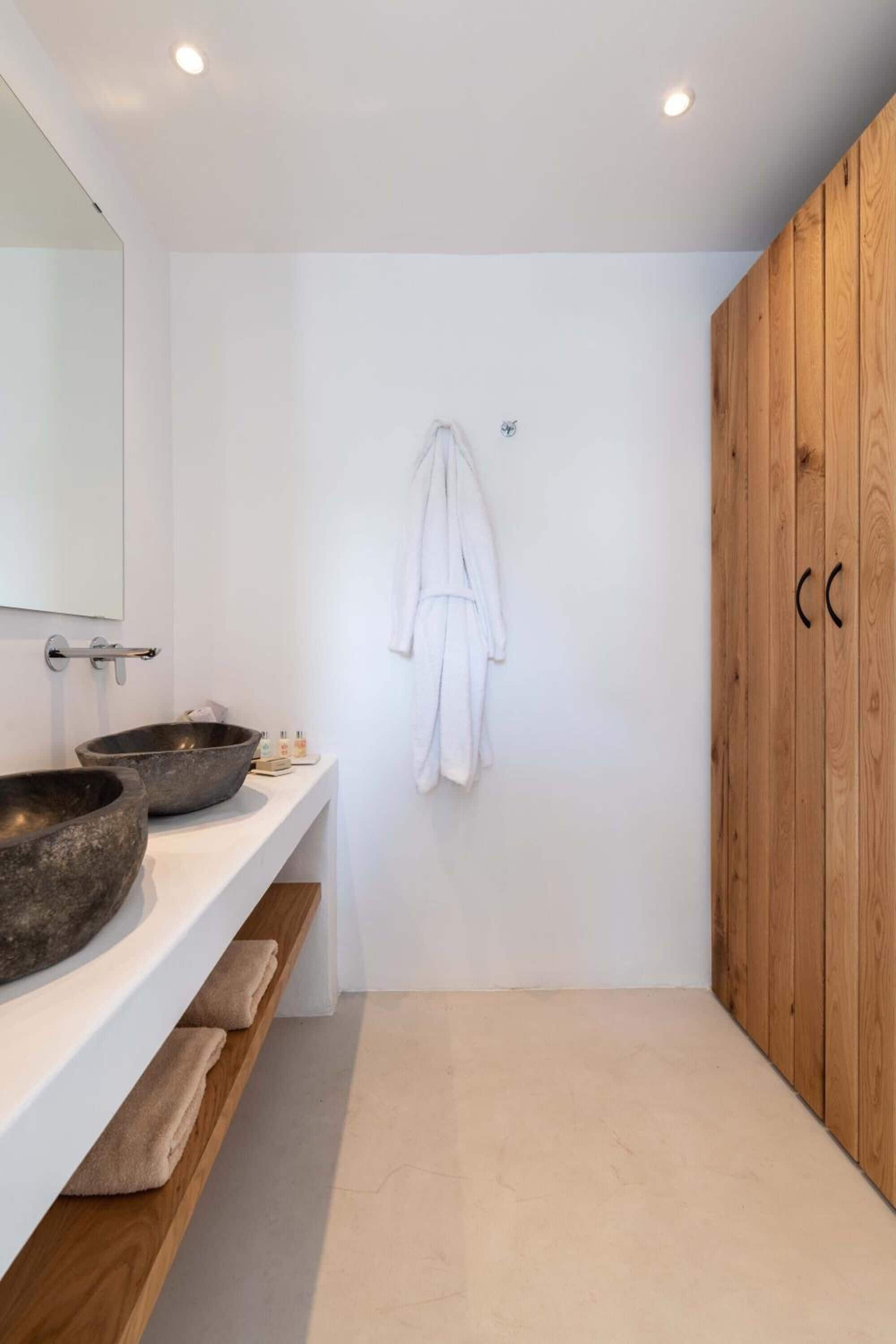 Ein modernes Badezimmer mit einem großen Spiegel, zwei Steinwaschbecken, Holzschränken und einem weißen Handtuchhalter.