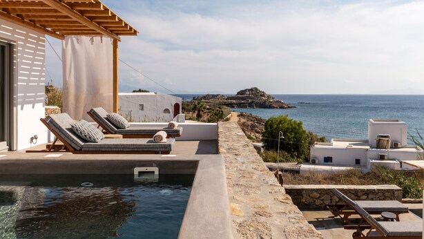 A poolside area with lounge chairs, a pergola, and a view of the sea. - Trinity Mykonos (Mykonos)