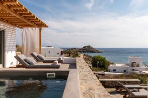 Ein Poolbereich mit Liegestühlen, einer Pergola und Blick auf das Meer.