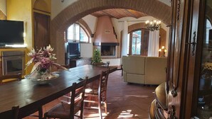Ein geräumiger Wohnbereich mit Kamin, Fernseher und Esstisch mit Stühlen.