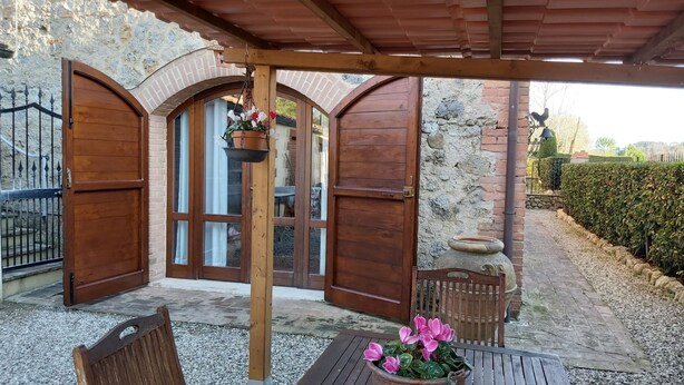Ein überdachter Patio-Bereich mit einer Holz-Pergola, einer Steinmauer und einem Kiesweg.