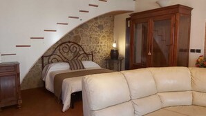Ein Schlafzimmer mit einer Steinsäule, einem Bett mit Kopfteil, einem Holzkabinent und einem beigefarbenen Sofa.