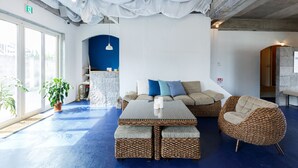 A modern interior with a blue floor, a sofa set, wicker chairs, and a large table. - Hostel NABLA (Niijima)
