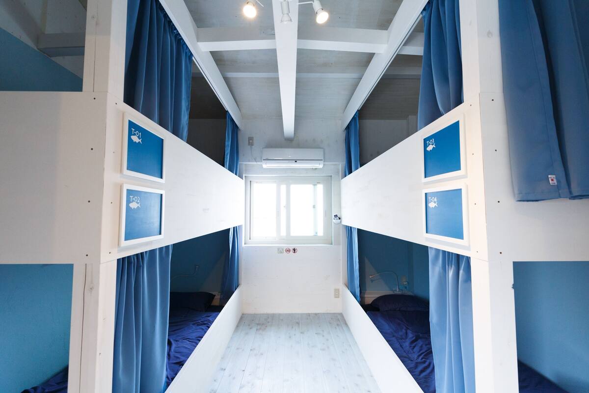 Ein schmales, fensterloses Zimmer mit Etagenbetten und Vorhängen.