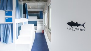A bunk room with blue curtains, a fire extinguisher, and a wall decal stating "ROOM 10 GUESTS". - Hostel NABLA (Niijima)