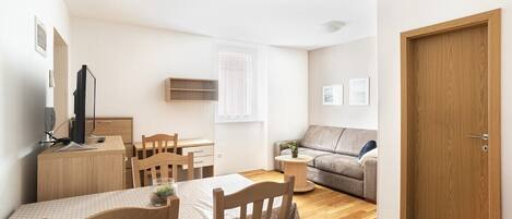 En kompakt opholdsstue med spiseplads, sofa, trædør og et lille bord med en plante.