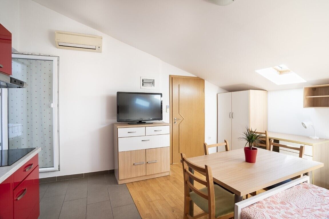 Una cocina compacta con televisión, armarios de madera, una mesa de comedor y un ventanal.