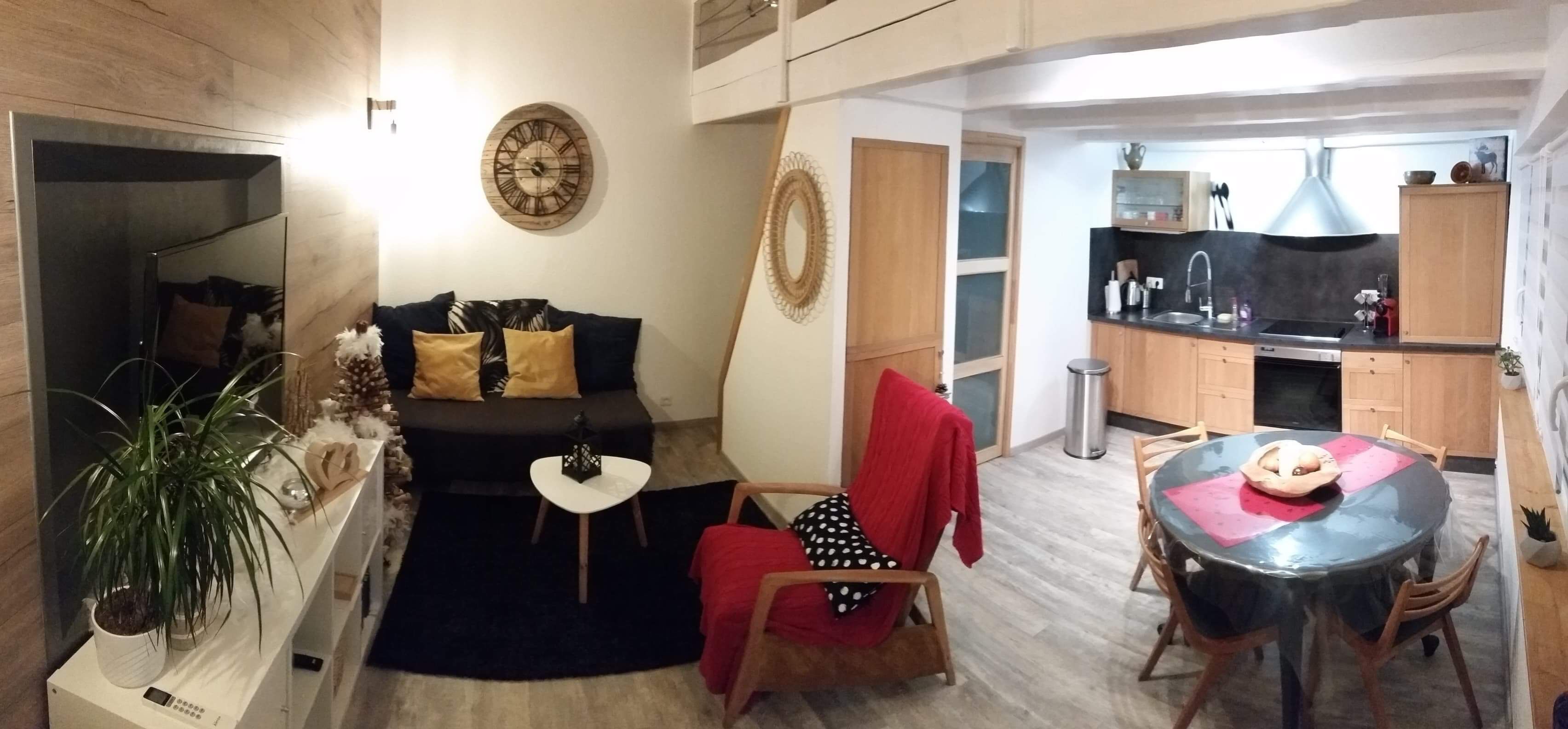A compact living space with a sofa, a small table, a dining table, and a kitchen area.
