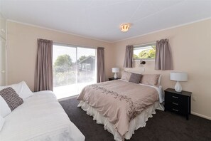 A bedroom with a large bed, two bedside tables with lamps, a window with curtains, and a view of the outside. - Hillside Heaven Quiet & Comfortable (Rotorua)