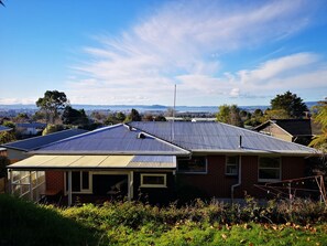 Uma casa residencial com telhado inclinado, painéis solares e vista para uma paisagem urbana e montanhas ao longe.