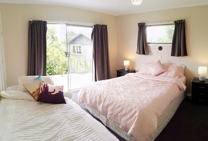 Quarto de hotel com duas camas, janela com cortinas, mesa de cabeceira com abajur e vista para áreas verdes.