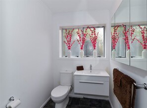 Casa de banho com sanita, lavatório e janela com flores cor-de-rosa.
