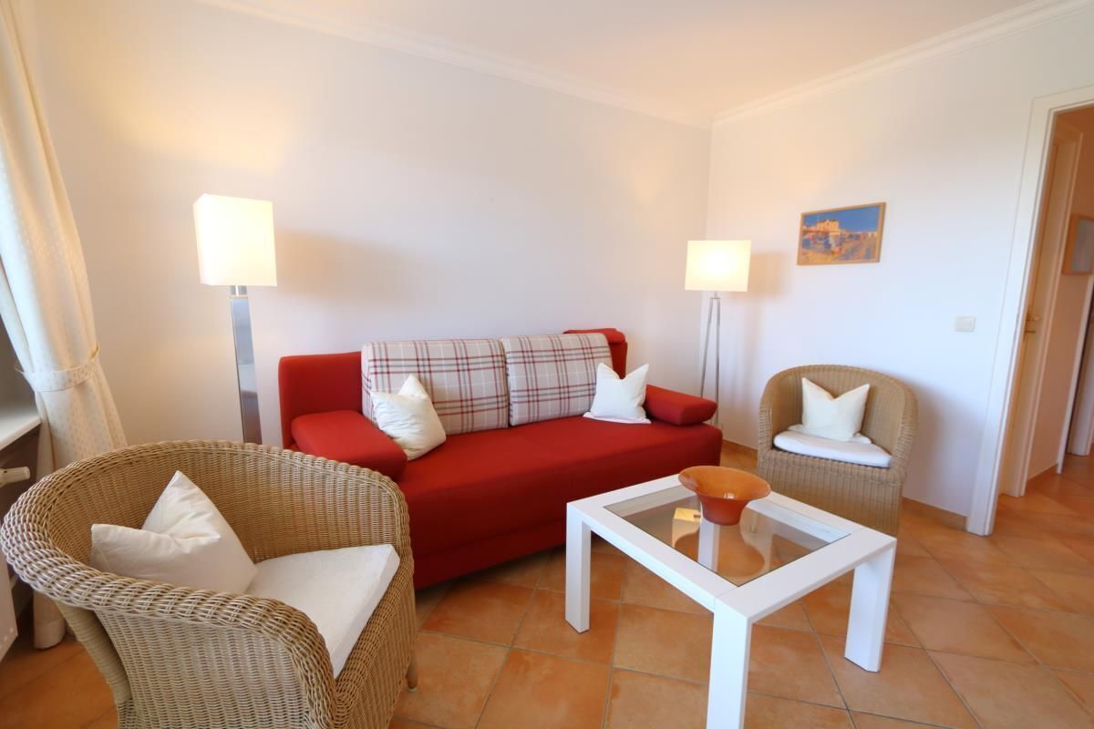 A living room with a red sofa, two wicker chairs, a white coffee table, and two floor lamps.