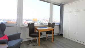 A room with a table and chairs, a window with a view of buildings, and a wardrobe. - App. Rüter 57, Germany (Sylt)