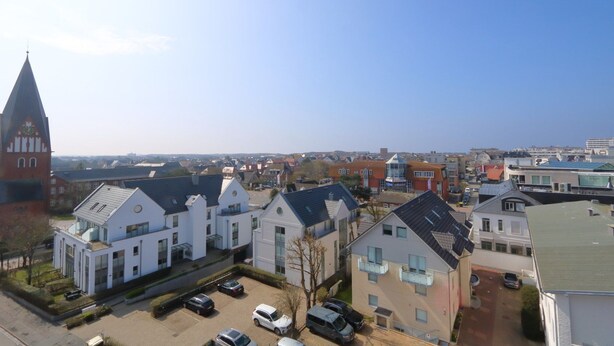 A residential area with modern houses, a church steeple, and a clear sky. - App. Rüter 57, Germany (Sylt)
