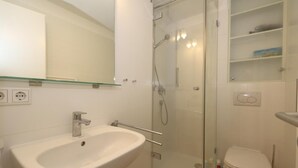 Ett modernt badrum med en dusch som är avskärmad med glasväggar, ett vitt handfat och en toalett.