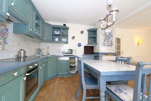 A kitchen with teal cabinets, a microwave, and a dining table with chairs. - Krauthahn Chimney, Germany (Sylt)