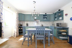 Une cuisine avec des meubles de couleur turquoise, un plan de travail recouvert de carreaux blancs et un îlot central doté de chaises.